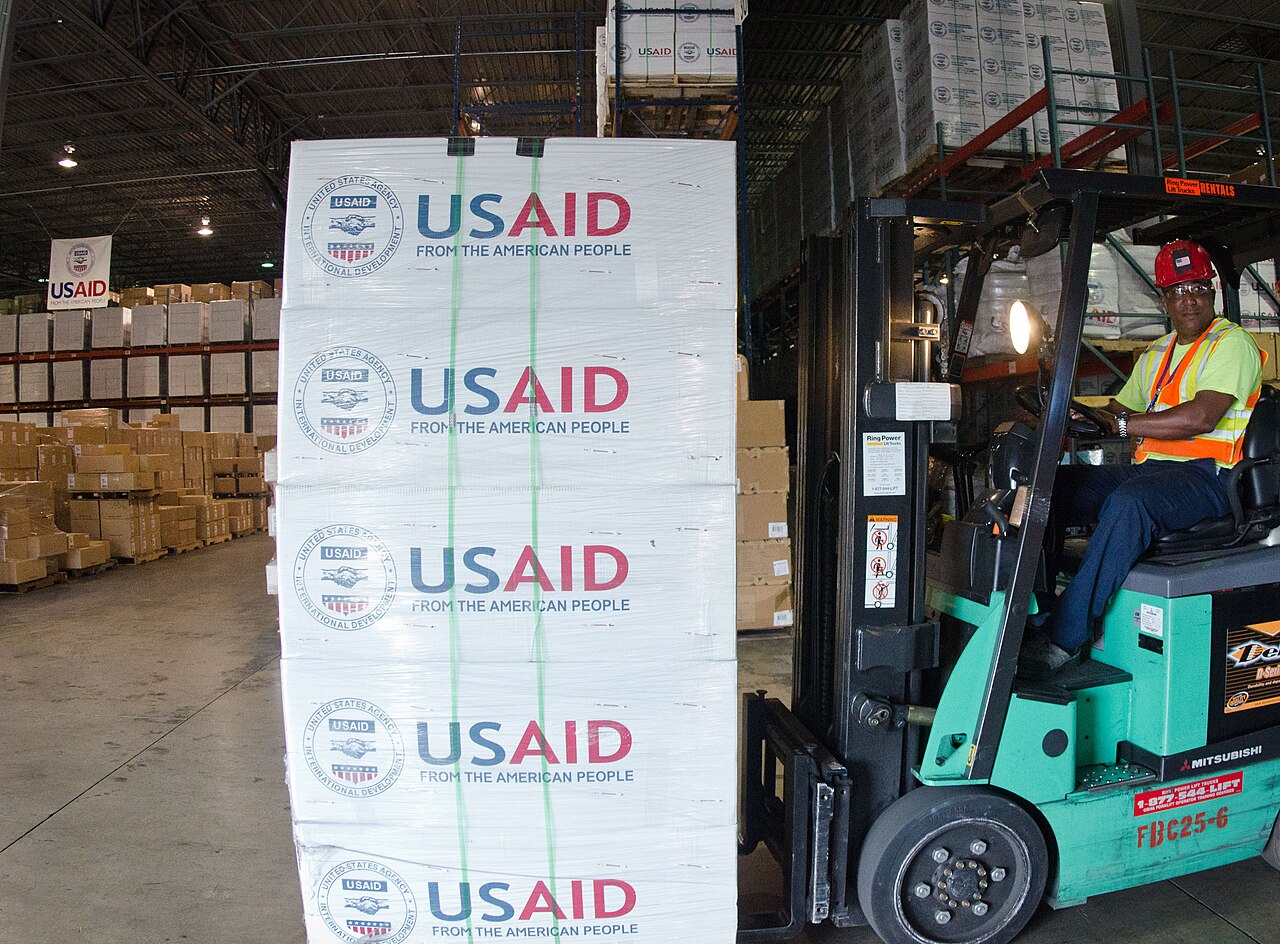 Workers driving forklifts loaded with goods inside a large warehouse