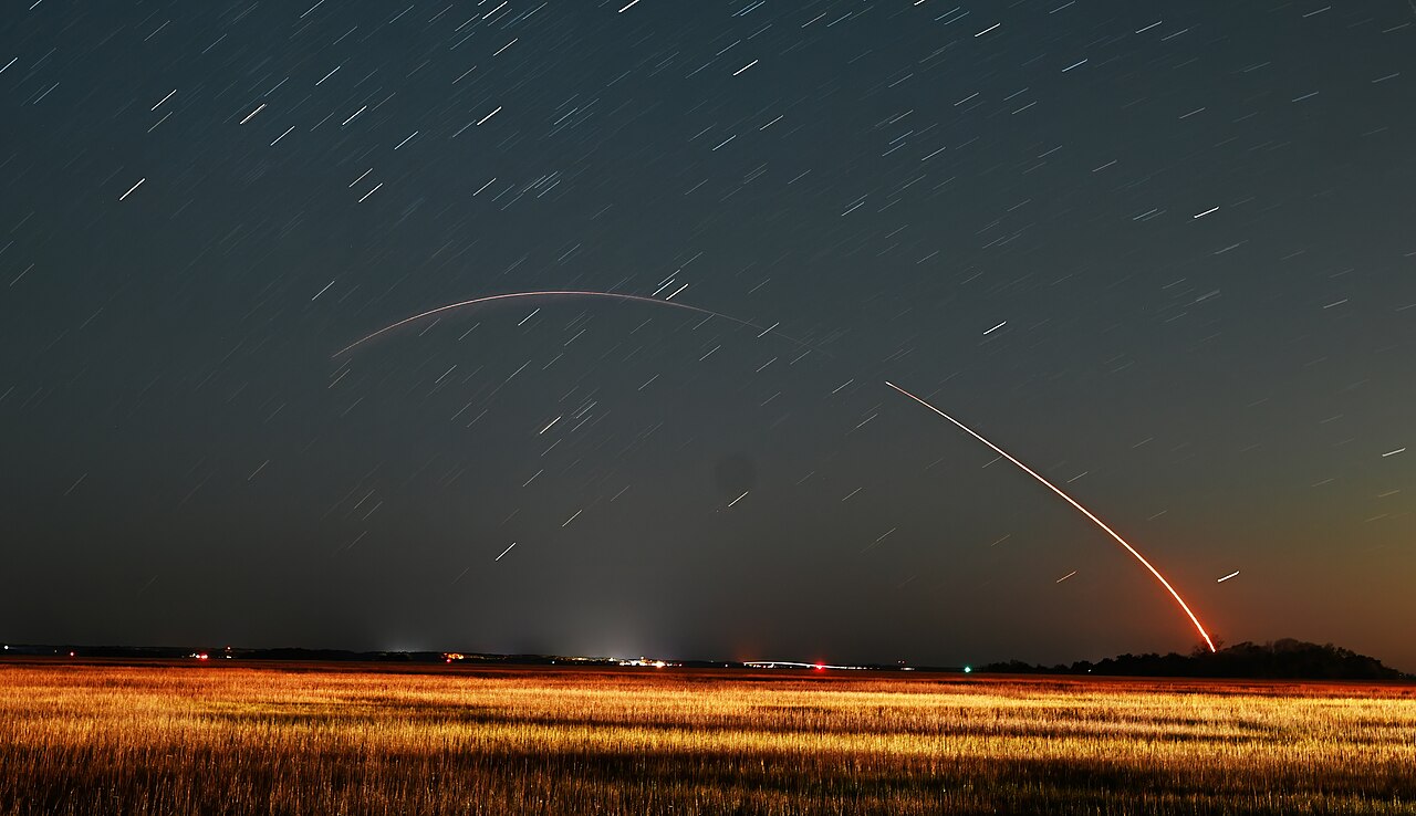 A rocket climbing into the night sky on a long trail of light
